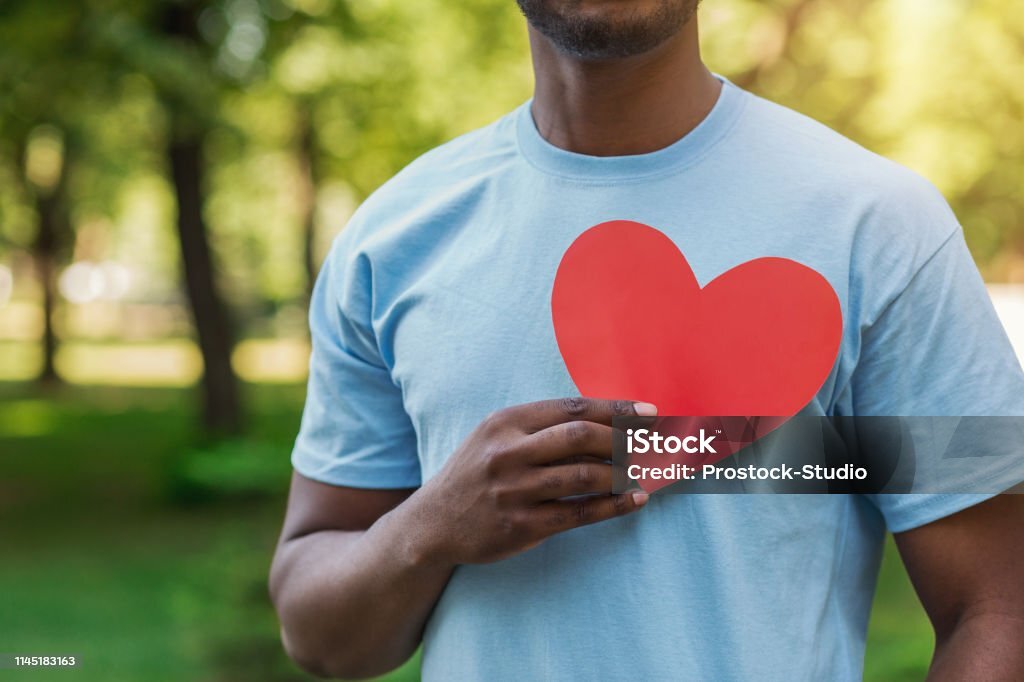 Love, volunteering and charity concept, copy space. Young black man holding red heart on his chest.